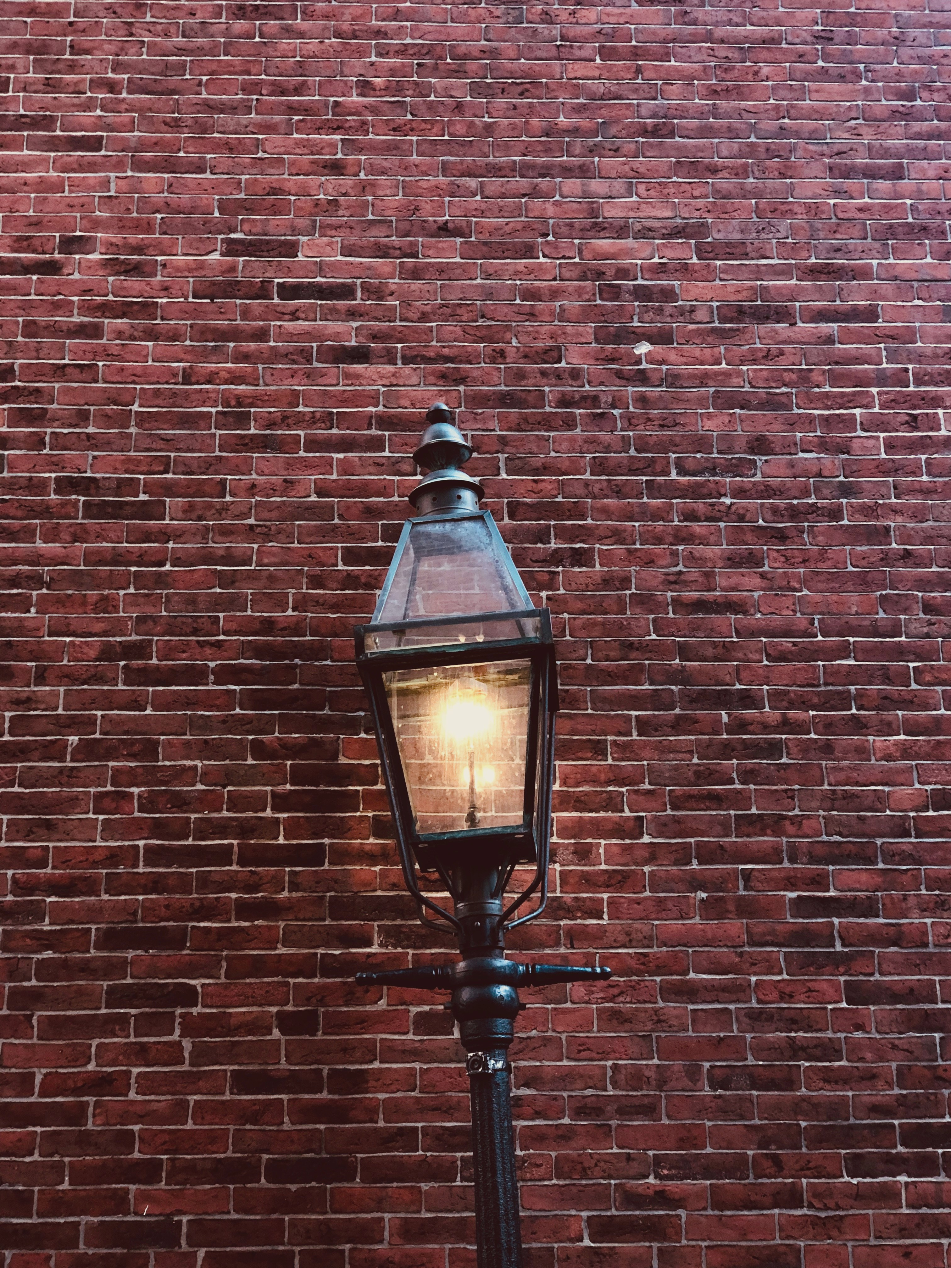 Unsplash. A photo of a lit streetlamp against a red brick background.