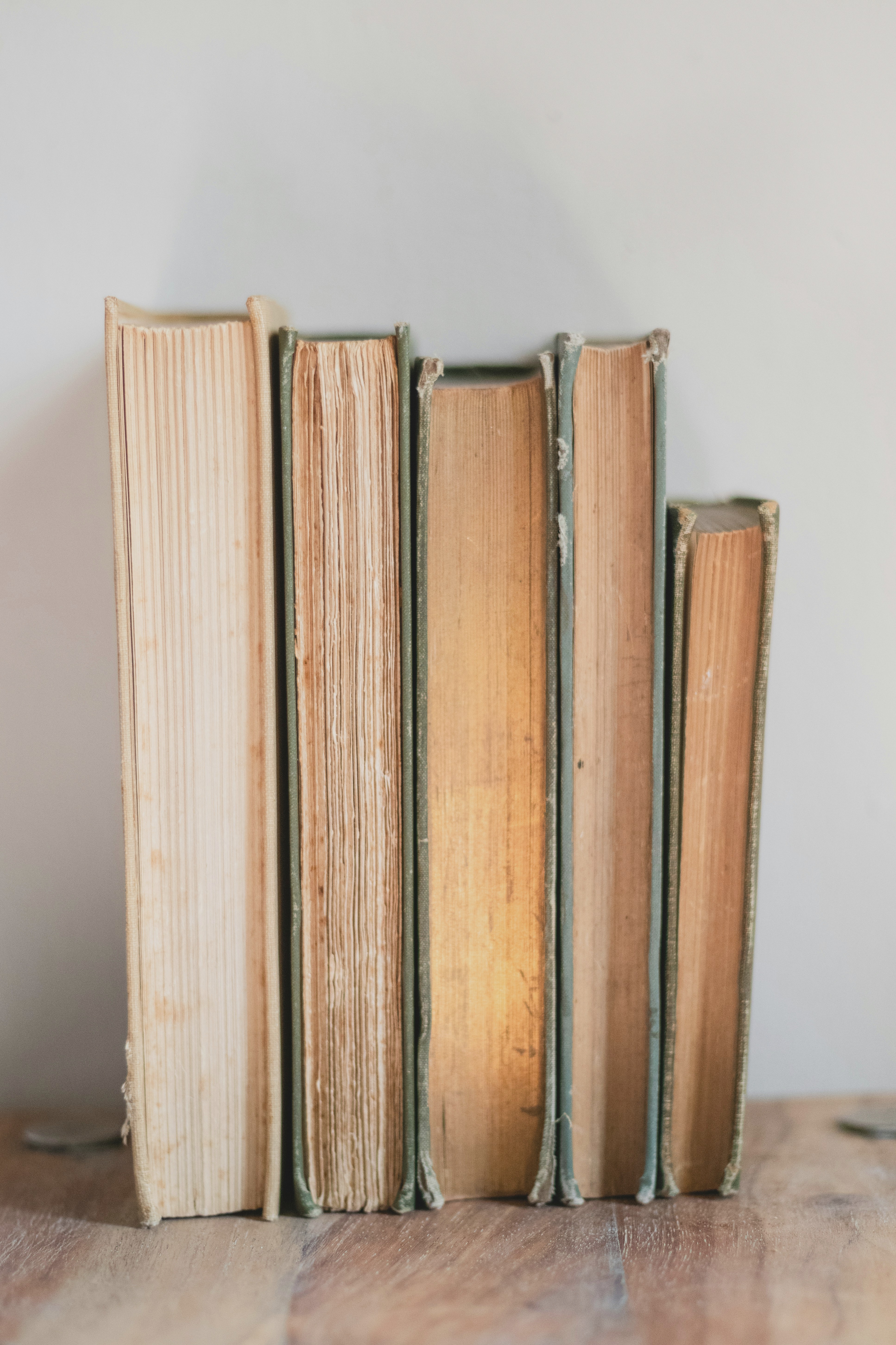 Unsplash. A photo of five books stacked vertically on a light wood surface with some coins in the background.